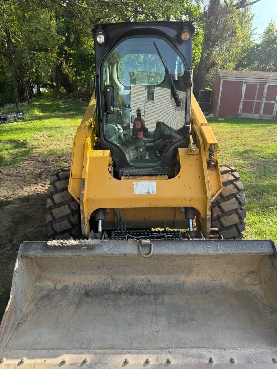 Yellow skid steer loader with a front bucket parked on grass in a backyard.