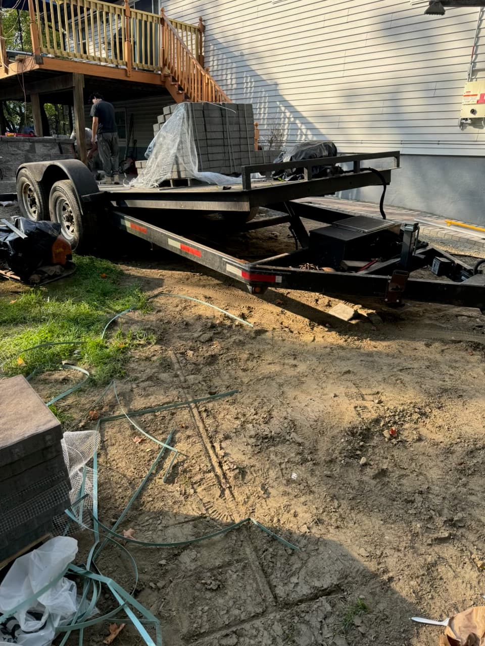 Black utility trailer loaded with grey paving stones parked on a dirt construction site.